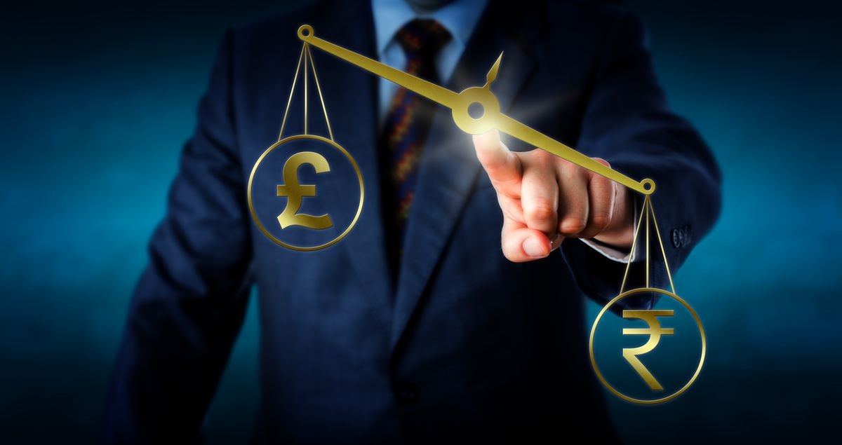 Indian rupee currency symbol is outbalancing the British pound sterling sign on a virtual golden pair of scales. Metaphor for trade imbalance and the modern foreign currency exchange market.